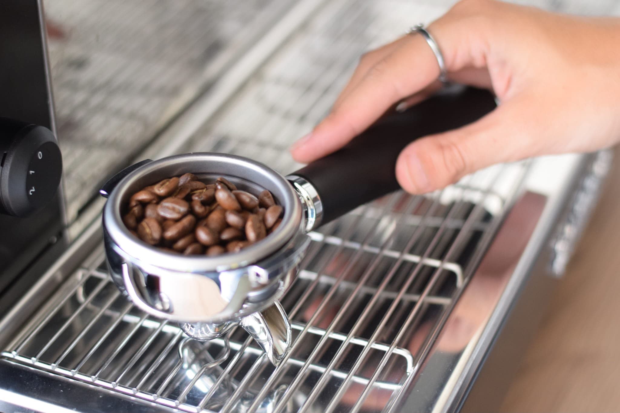 Een hand met de filterhouder vol verse koffiebonen boven het rooster van de espressomachine