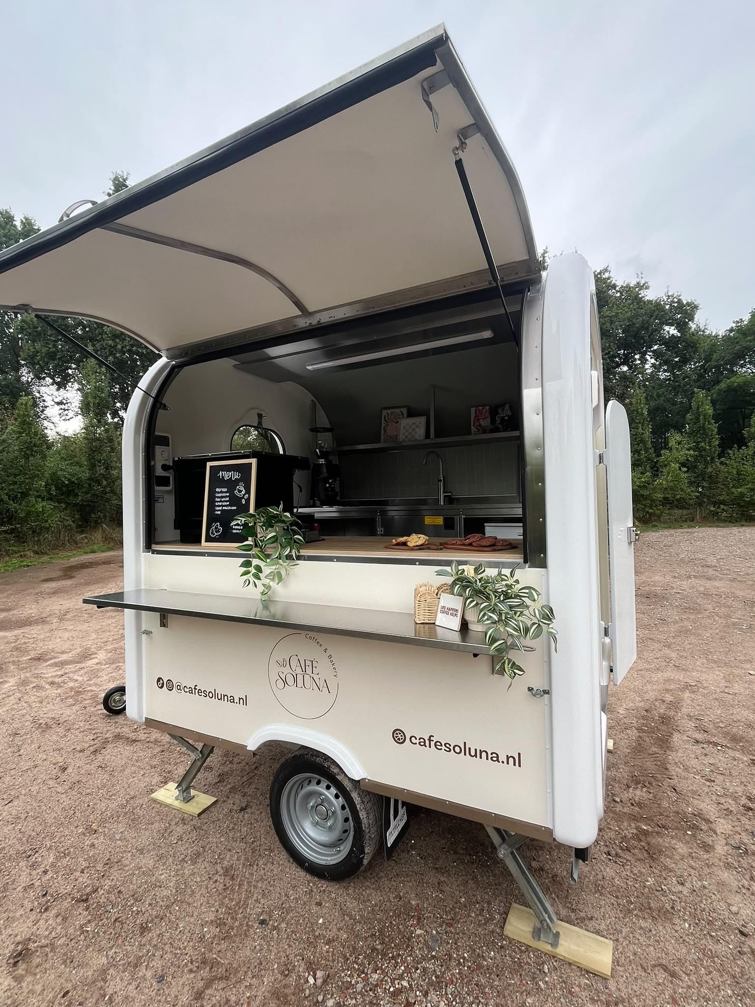 De foodtruck van Café Soluna open op een erf, met het dak omhoog, het menubord binnen en het logo op de zijkant