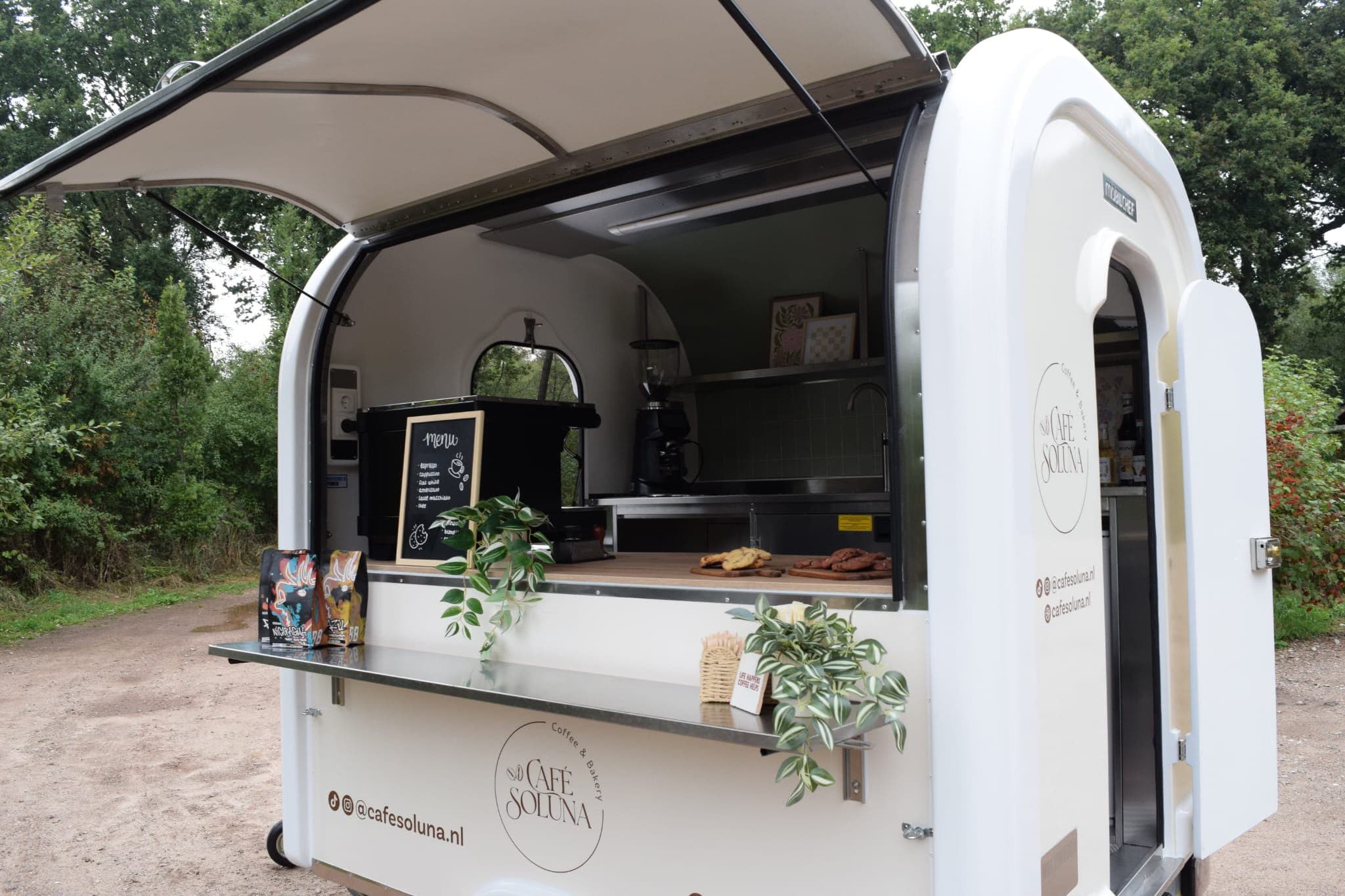 De foodtruck open op een pad in het bos, met het dak omhoog en zakken koffie op de toonbank